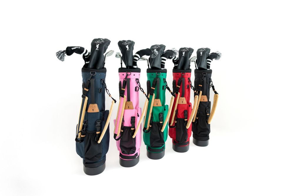 Five colorful mini golf bags in navy, pink, green, red, and burgundy with clubs, displayed in a row on white background.