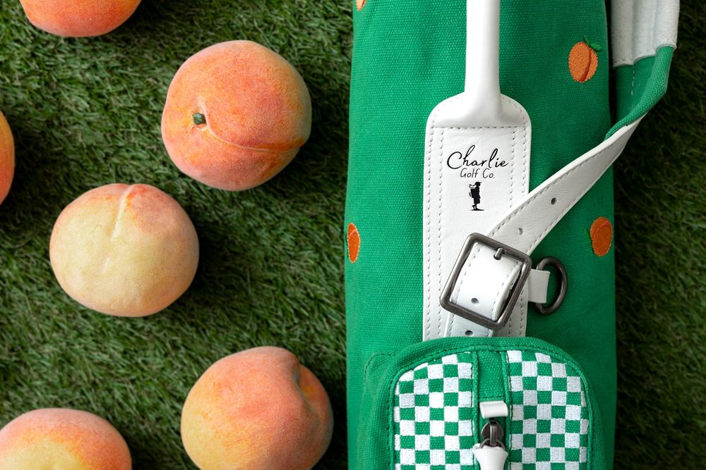 Fresh peaches arranged on artificial green grass next to green and white decorative bottles.