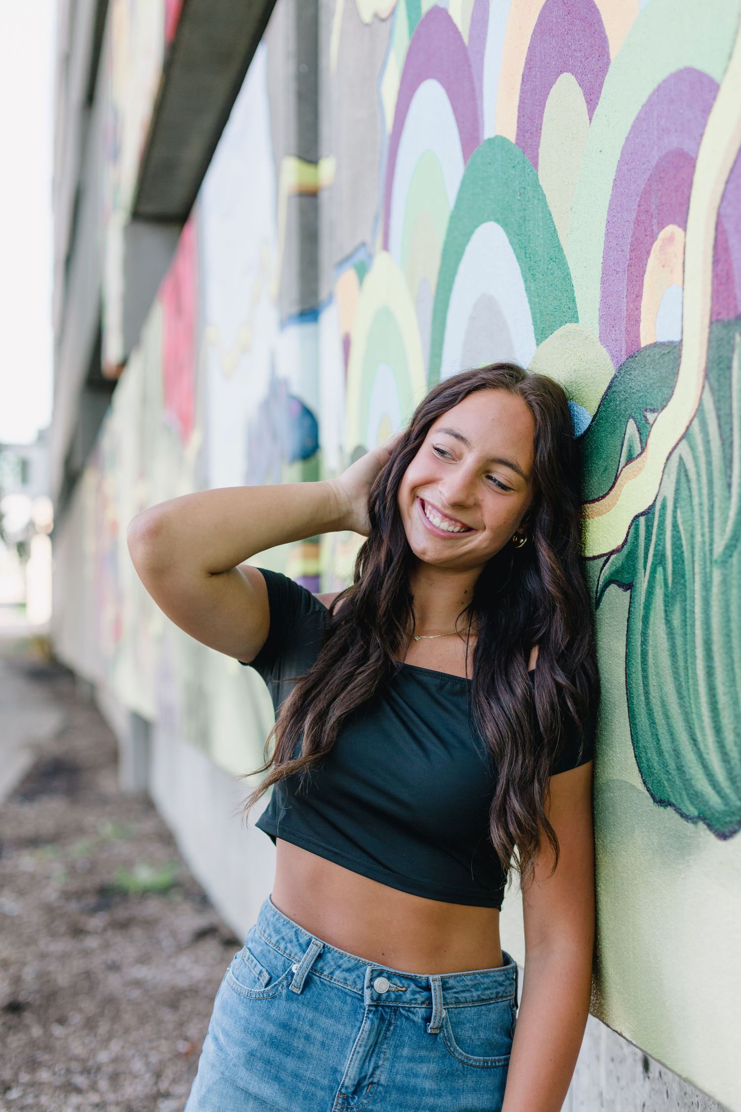 A joyful moment captured against a colorful mural wall, wearing a dark crop top and blue jeans.