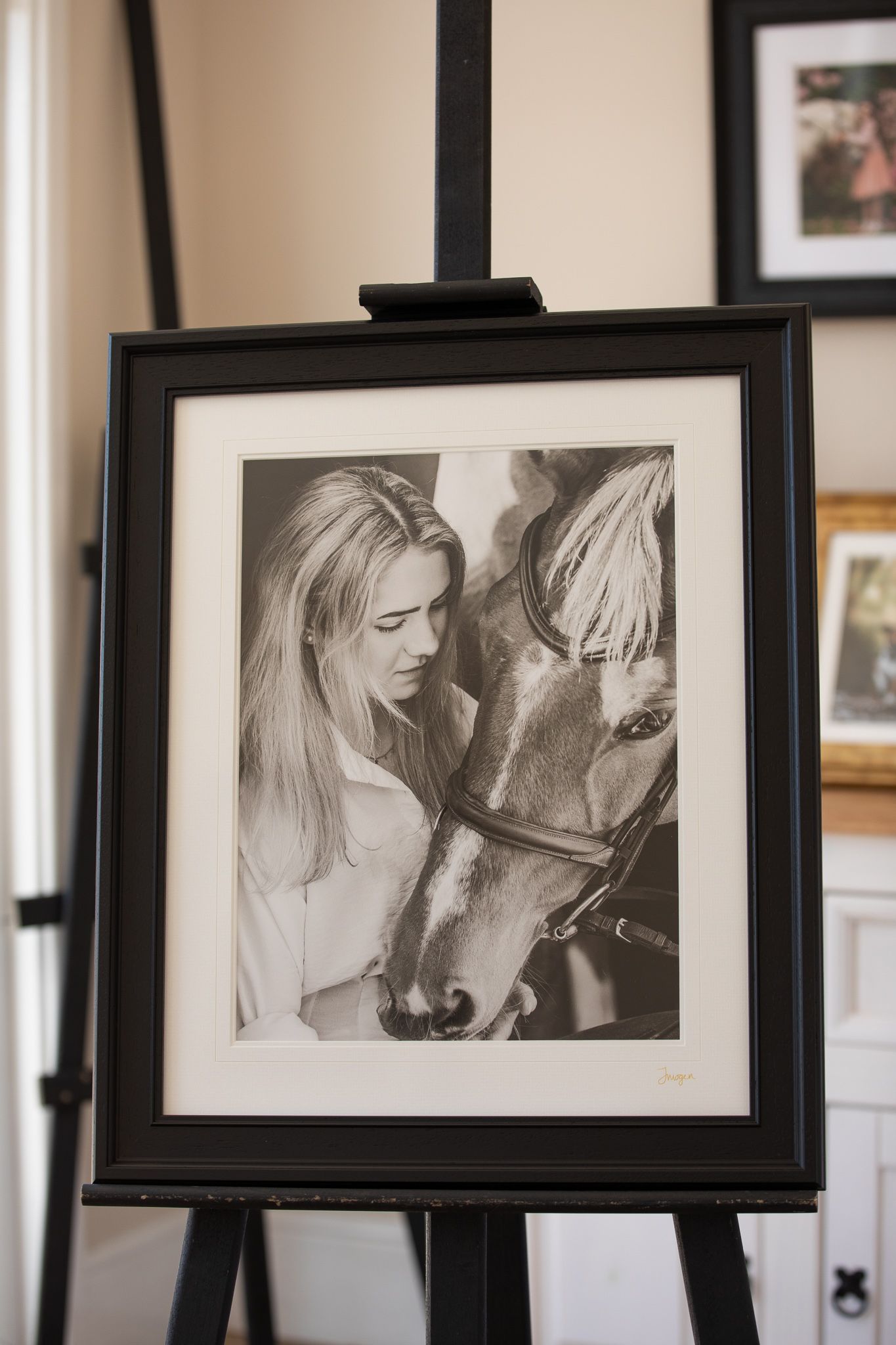 A black and white framed photograph displayed on an easel shows a tender moment between a woman and a horse.