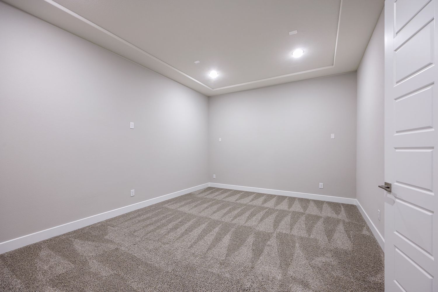 Empty carpeted room with grey walls, white baseboards, and recessed lighting in the ceiling.