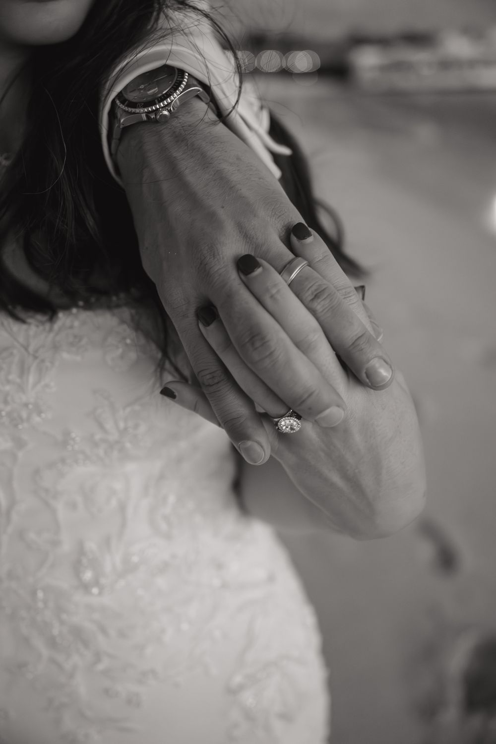 Close-up black and white image of hands displaying an elegant engagement ring with diamond solitaire.