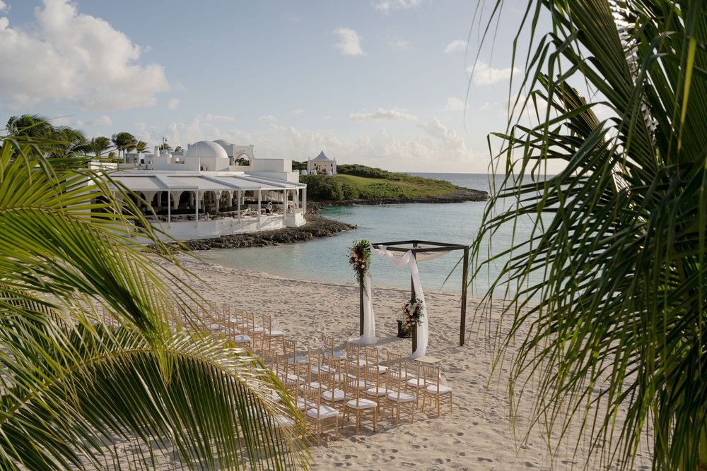Beach wedding ceremony setup with white chairs and tropical oceanfront view.