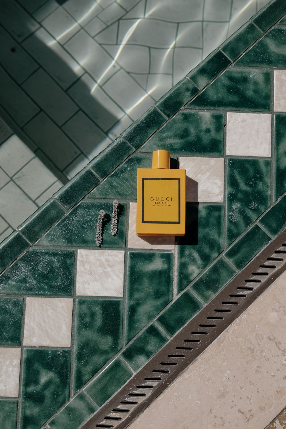Abstract geometric pattern with yellow Gucci perfume bottle on white and green tiled surface.