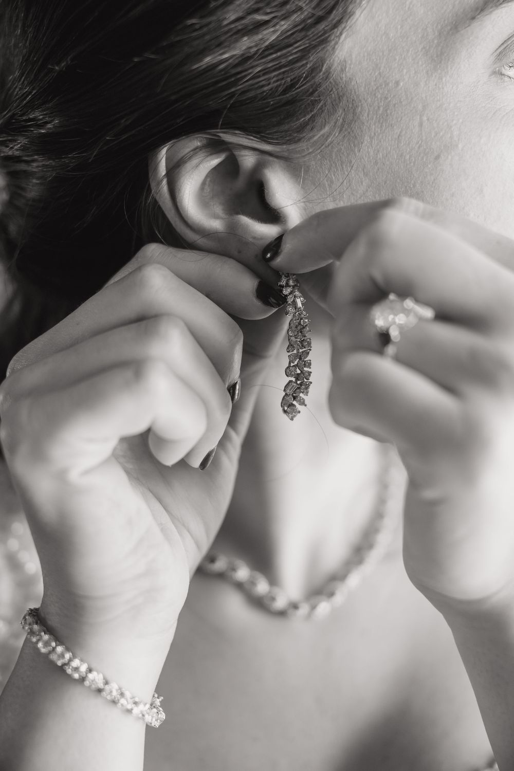 Hands putting on an elegant crystal drop earring with pearl bracelet and diamond ring.