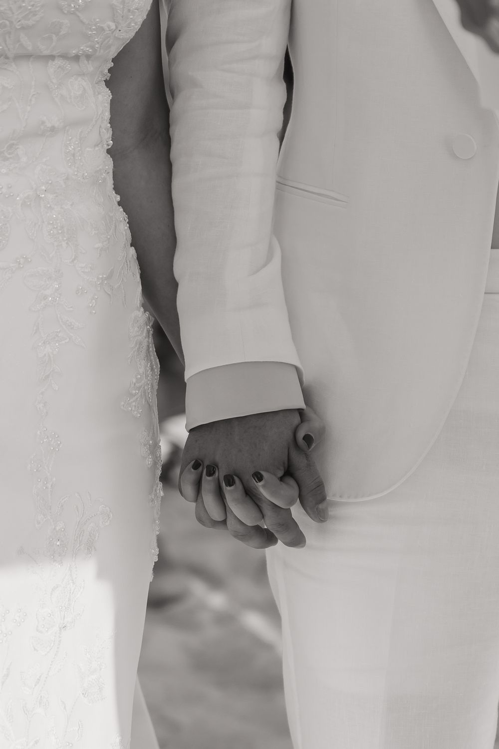 Black and white photo of couple holding hands in formal wedding attire.