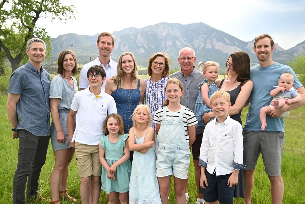 A group stands together outdoors with scenic mountain peaks in the background on a sunny day.
