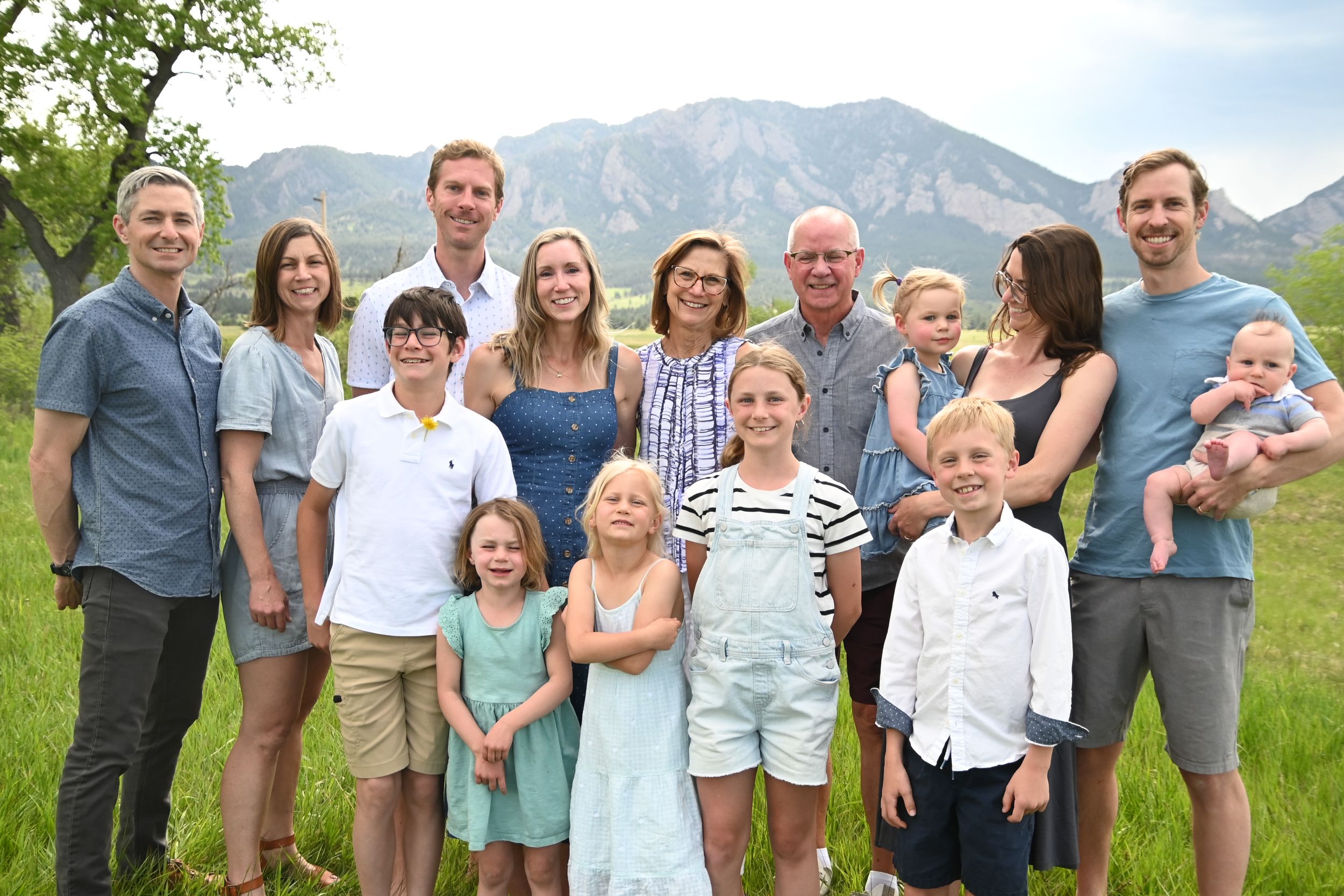 A group stands together outdoors with scenic mountain peaks in the background on a sunny day.