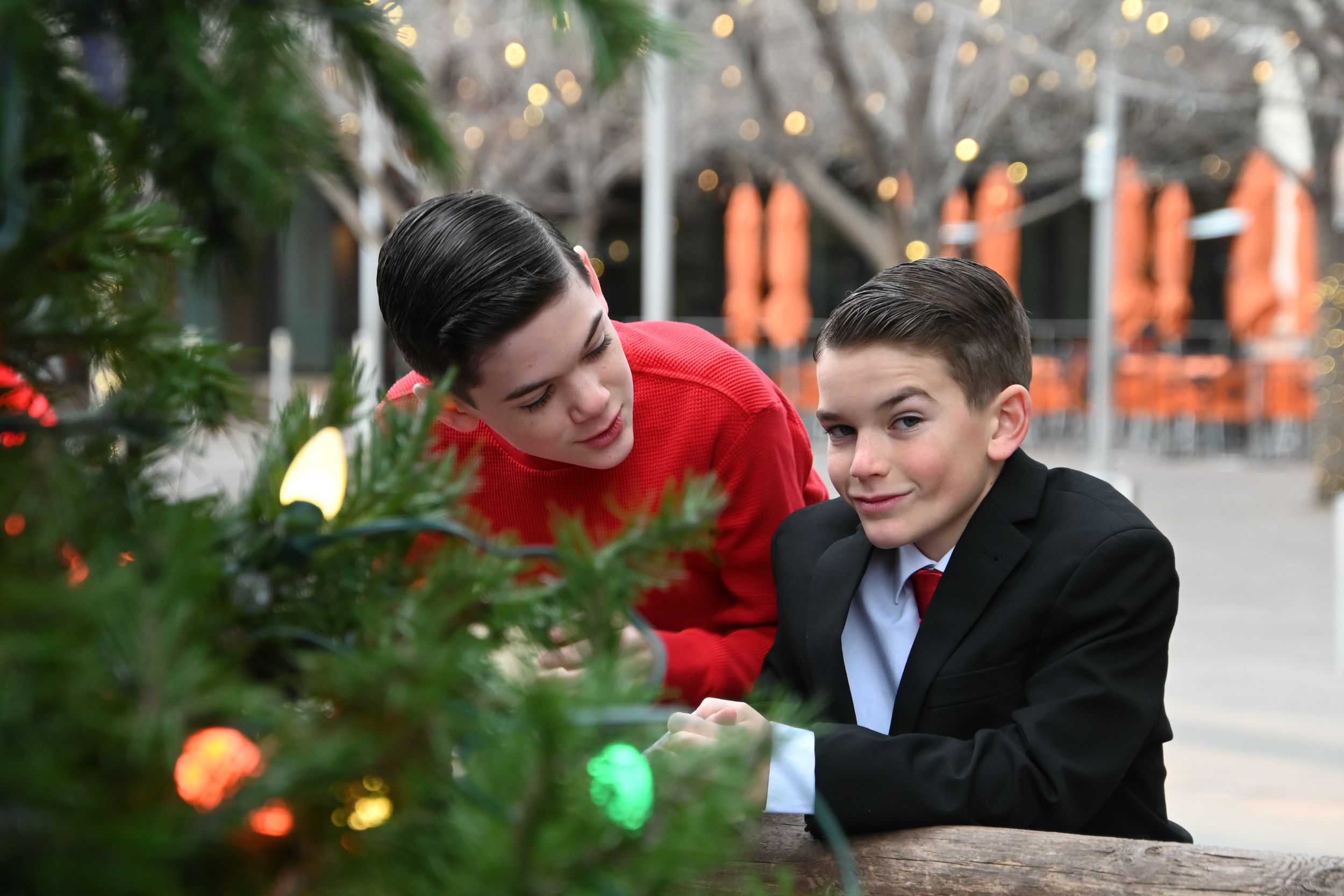 Two people look at Christmas decorations together among twinkling holiday lights and greenery.