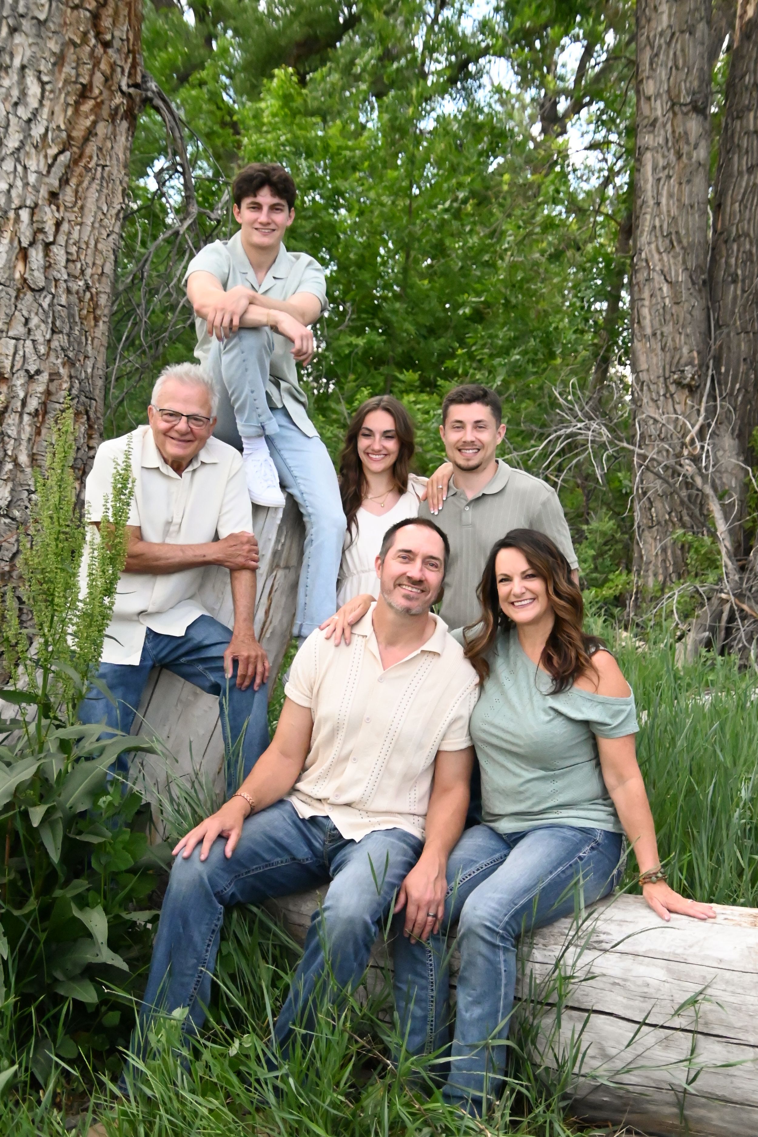 Family of six posing together while sitting on a fallen log outdoors with trees in the background.