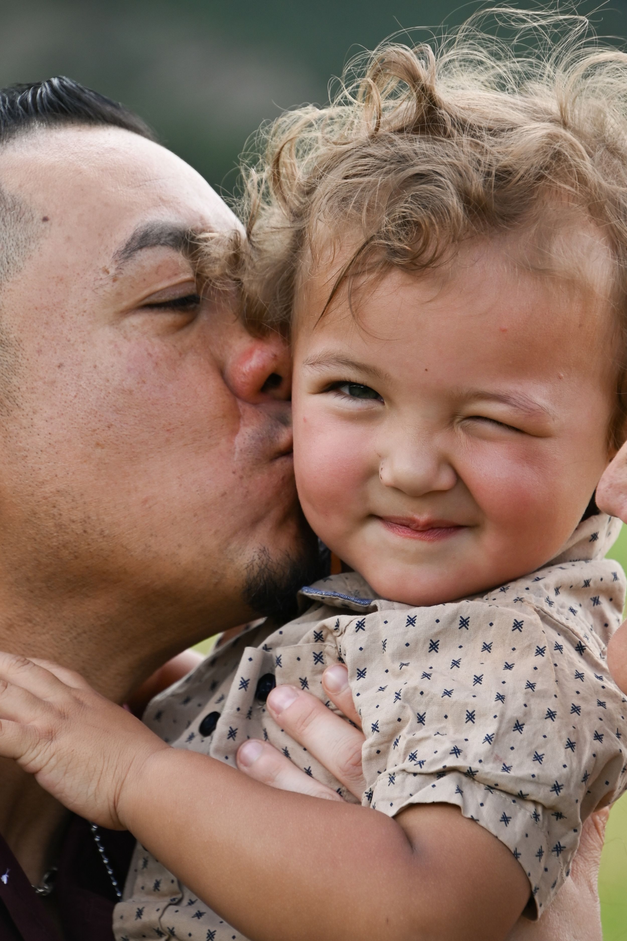 Tender moment captured as a parent gives child a kiss on the cheek, making them smile with joy and scrunch their nose.