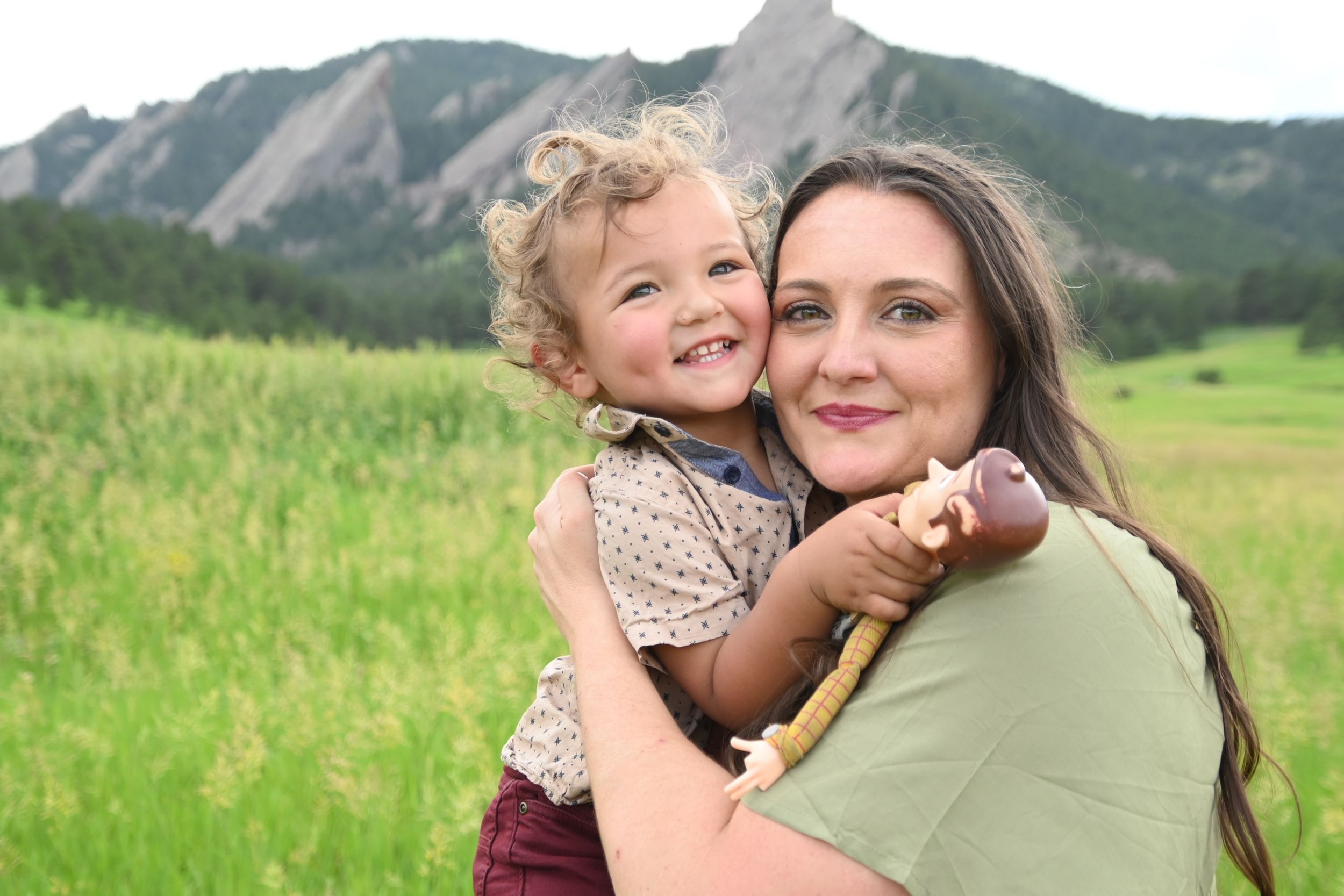 A joyful embrace captured in a grassy field with the iconic Flatirons rock formations of Boulder, Colorado in the background.
