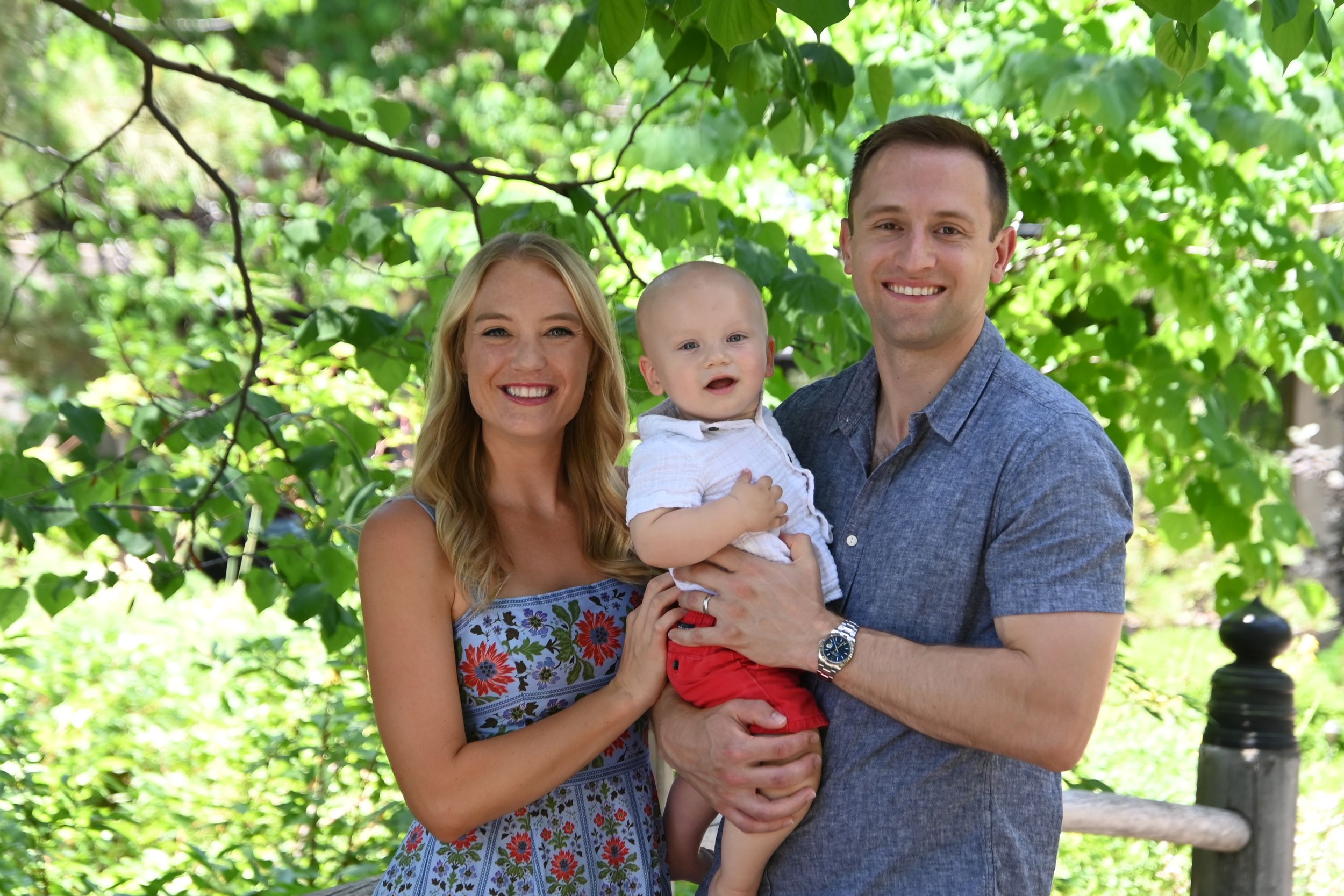 A family shares loving moments together while posing in front of lush green foliage during a summer photo session.