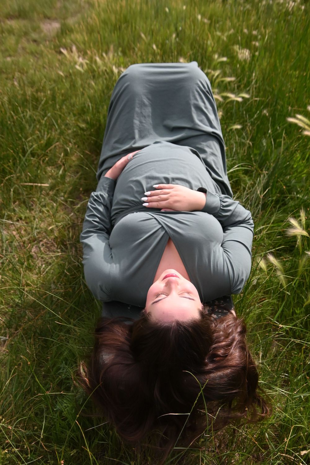 Someone wearing a grey sweater lies peacefully in tall grass during a tranquil moment outdoors.