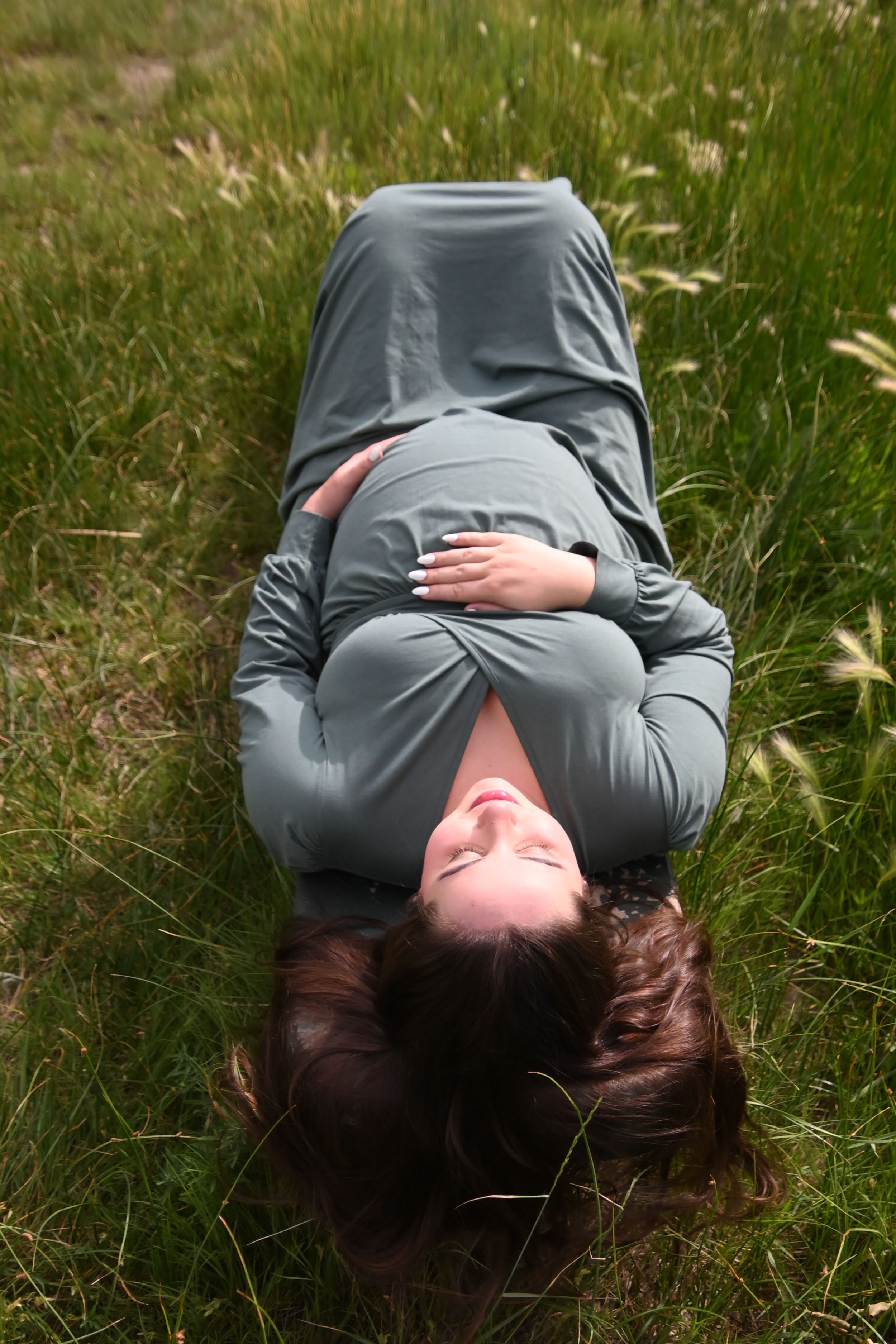 Someone wearing a grey sweater lies peacefully in tall grass during a tranquil moment outdoors.