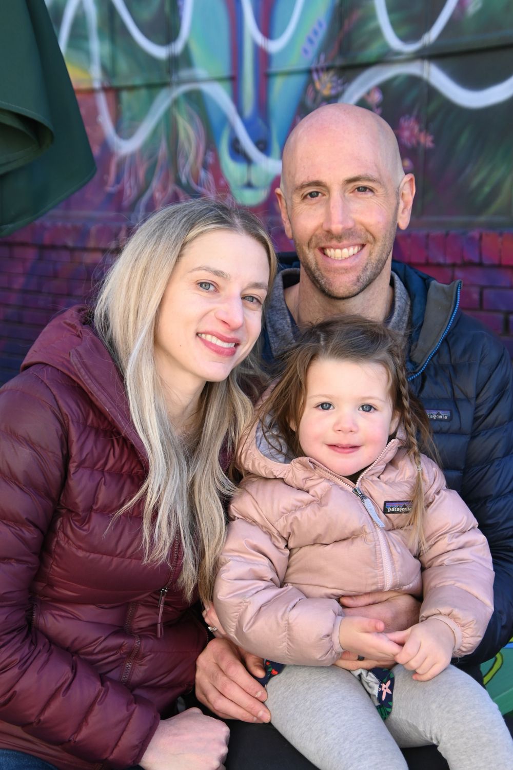Family wearing warm winter coats poses together against colorful graffiti wall in outdoor photo series.