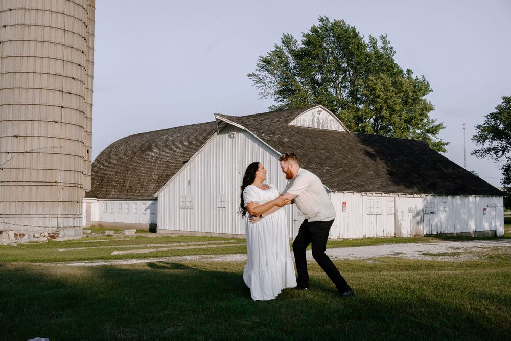 Two figures in formal attire pose together for wedding photographs in front of a rustic farm silo.