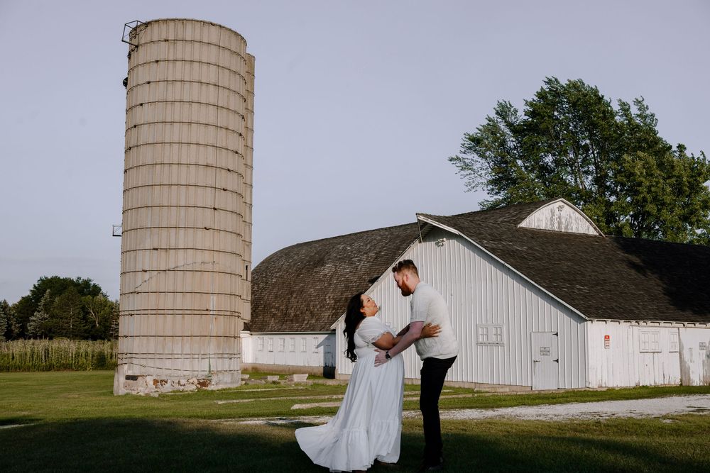 A couple shares a romantic moment by a rustic barn and silo on a farm during a wedding photoshoot.