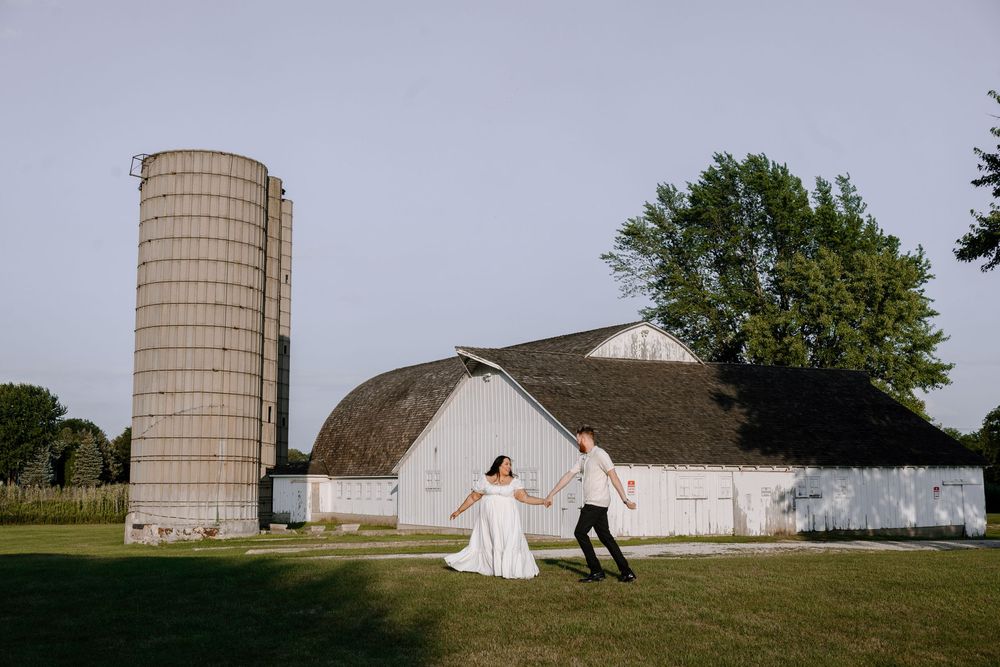A flowing white wedding dress twirls against the backdrop of a vintage barn and silo at sunset.