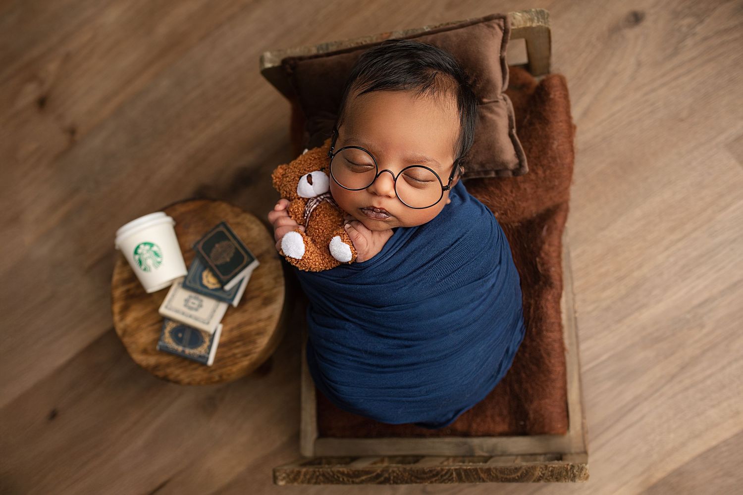 A baby rests on a wooden floor next to a small wooden box containing various items.