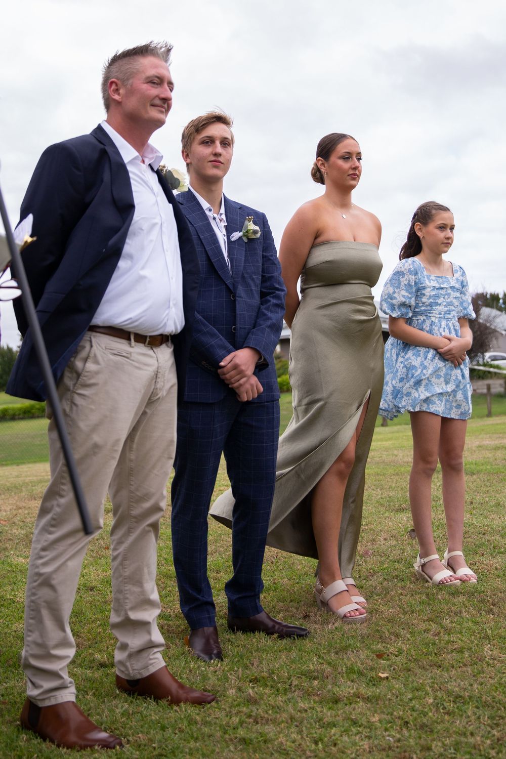 Low angle shot showing legs and feet of wedding party members standing on grass at an outdoor event.