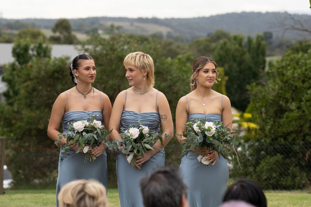 Row of bridesmaids in gray dresses holding white floral bouquets against a scenic mountain backdrop.