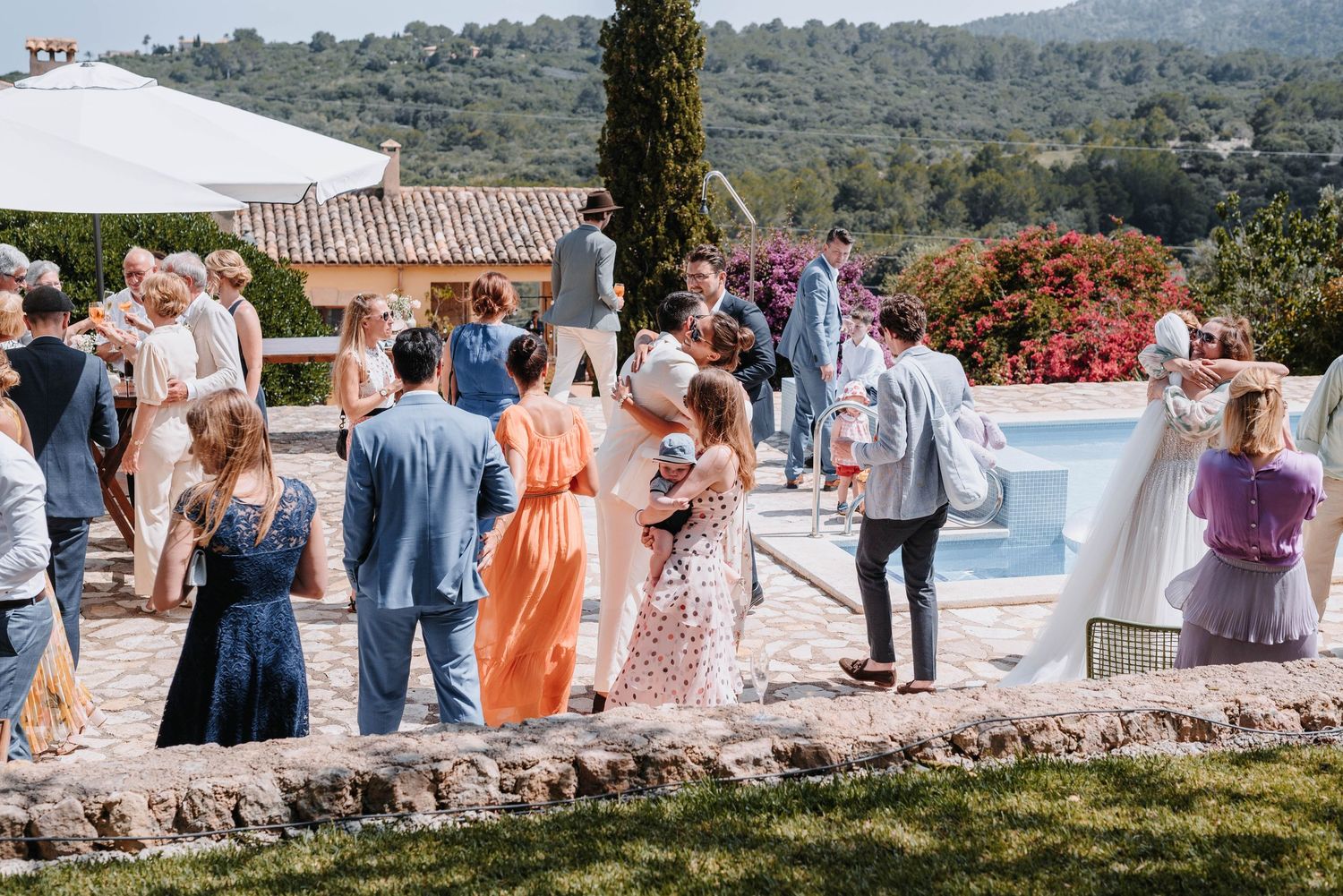 Die Gäste versammeln sich zu einem Empfang im Freien an einem Pool mit Blick auf die Landschaft Mallorcas und mediterraner Architektur.