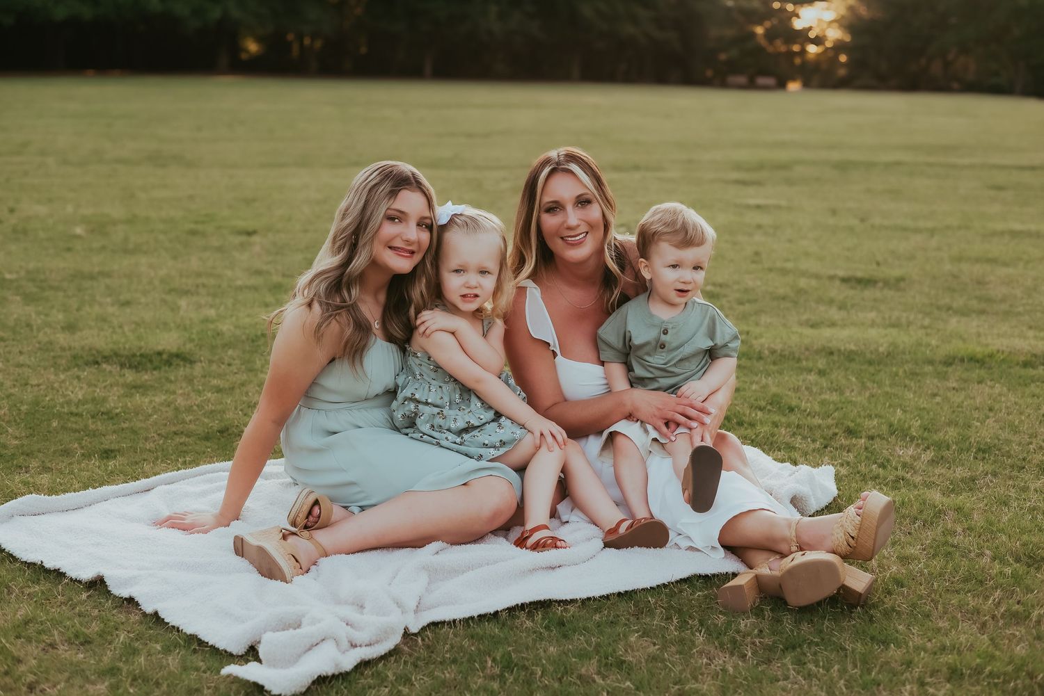 Small group relaxing on white blanket in grassy field during golden hour.
