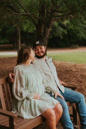 Couple sharing intimate moment while sitting on wooden bench under trees.