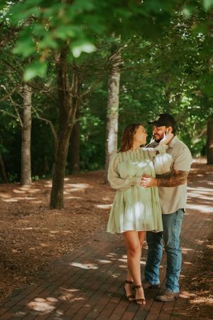 Couple embracing on brick pathway surrounded by trees.