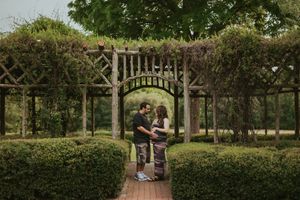 Couple standing under wooden garden arbor with climbing vines.