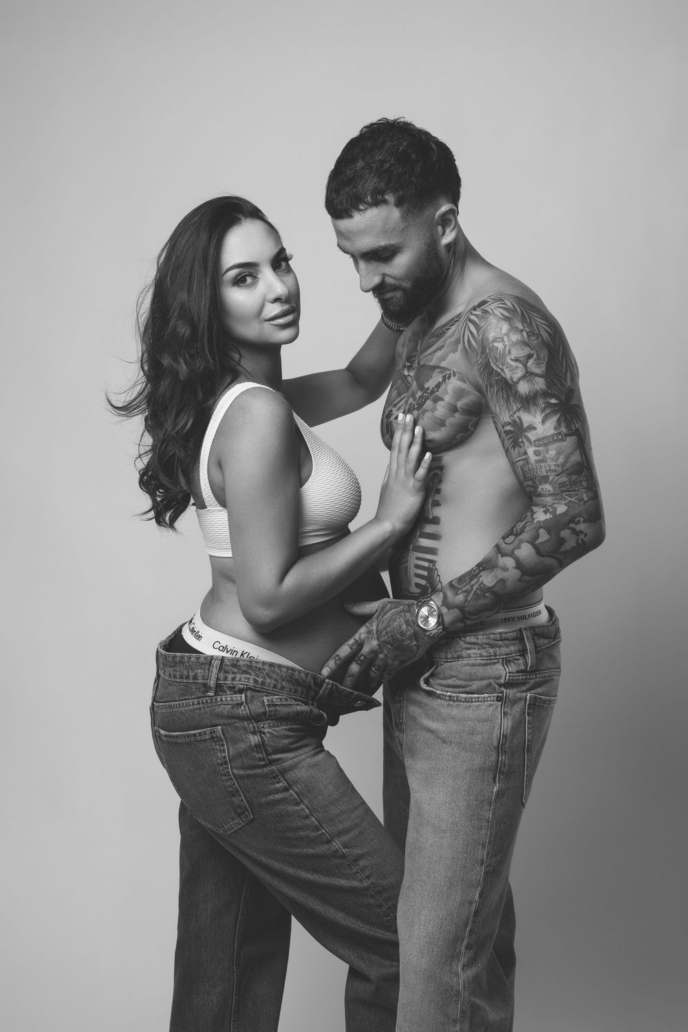 Black and white photo series showing intimate couple embracing, with woman in jeans and man with tattoos in multiple poses.