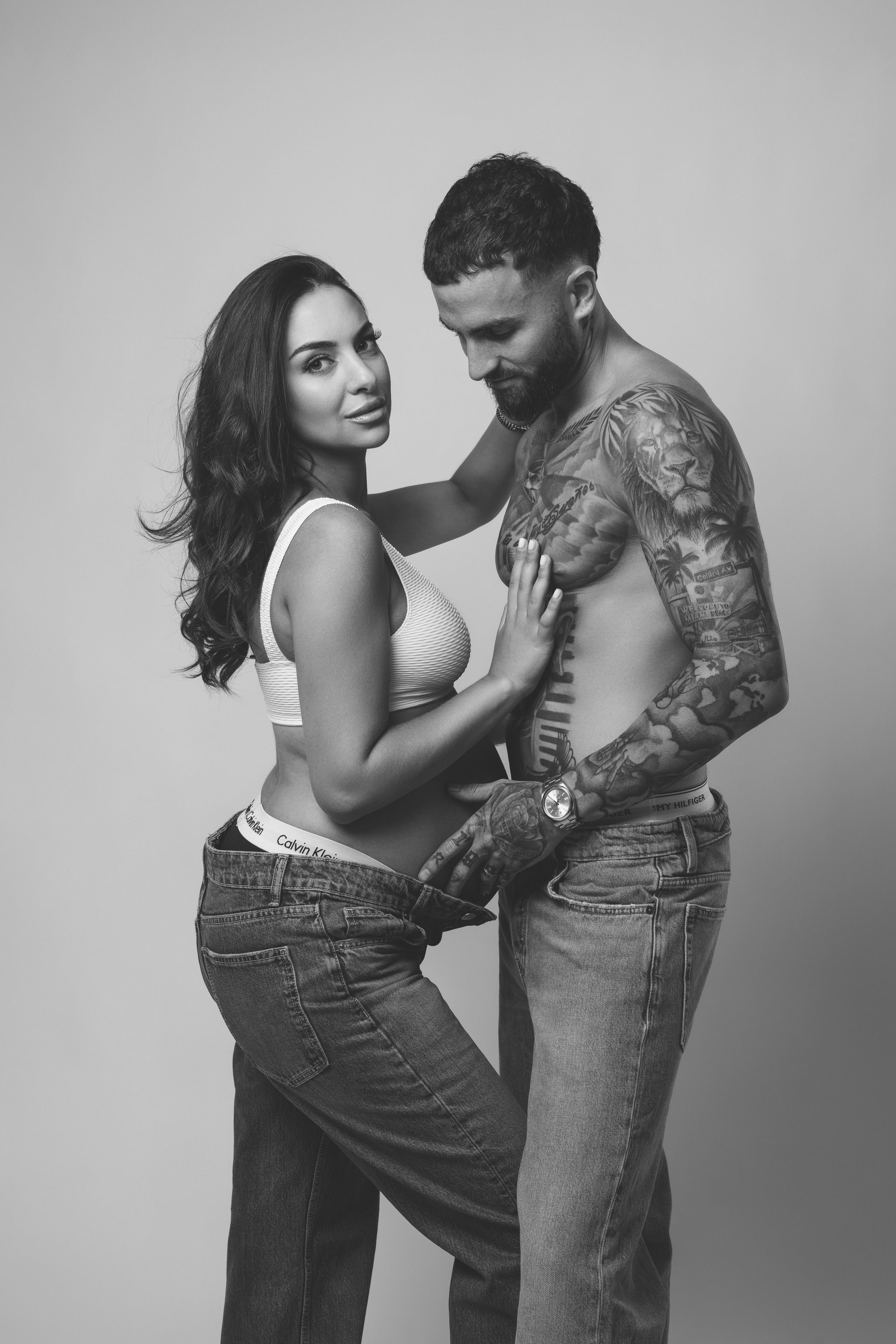 Black and white photo series showing intimate couple embracing, with woman in jeans and man with tattoos in multiple poses.