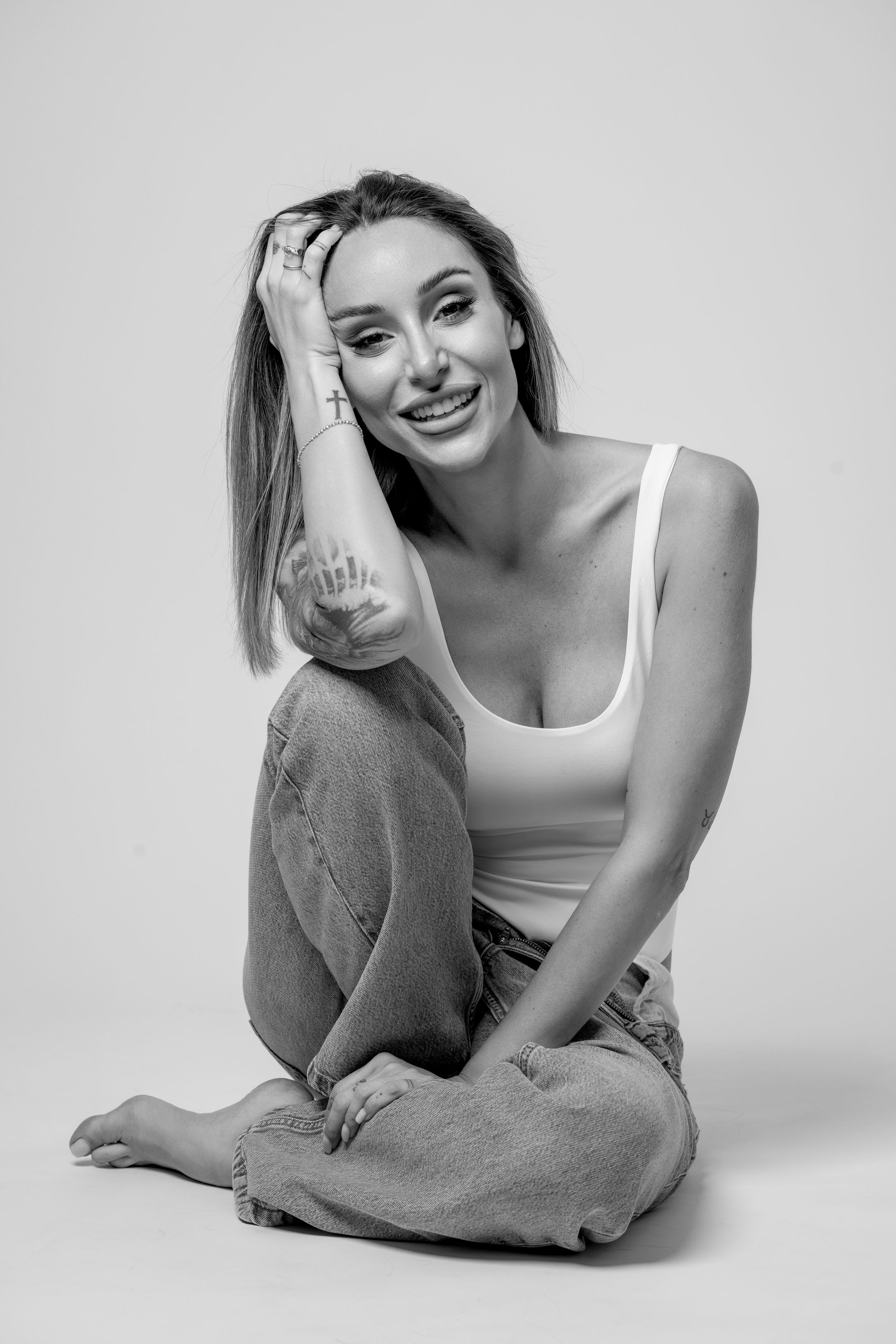 A woman in a white tank top poses casually against a light background in a series of relaxed portraits.