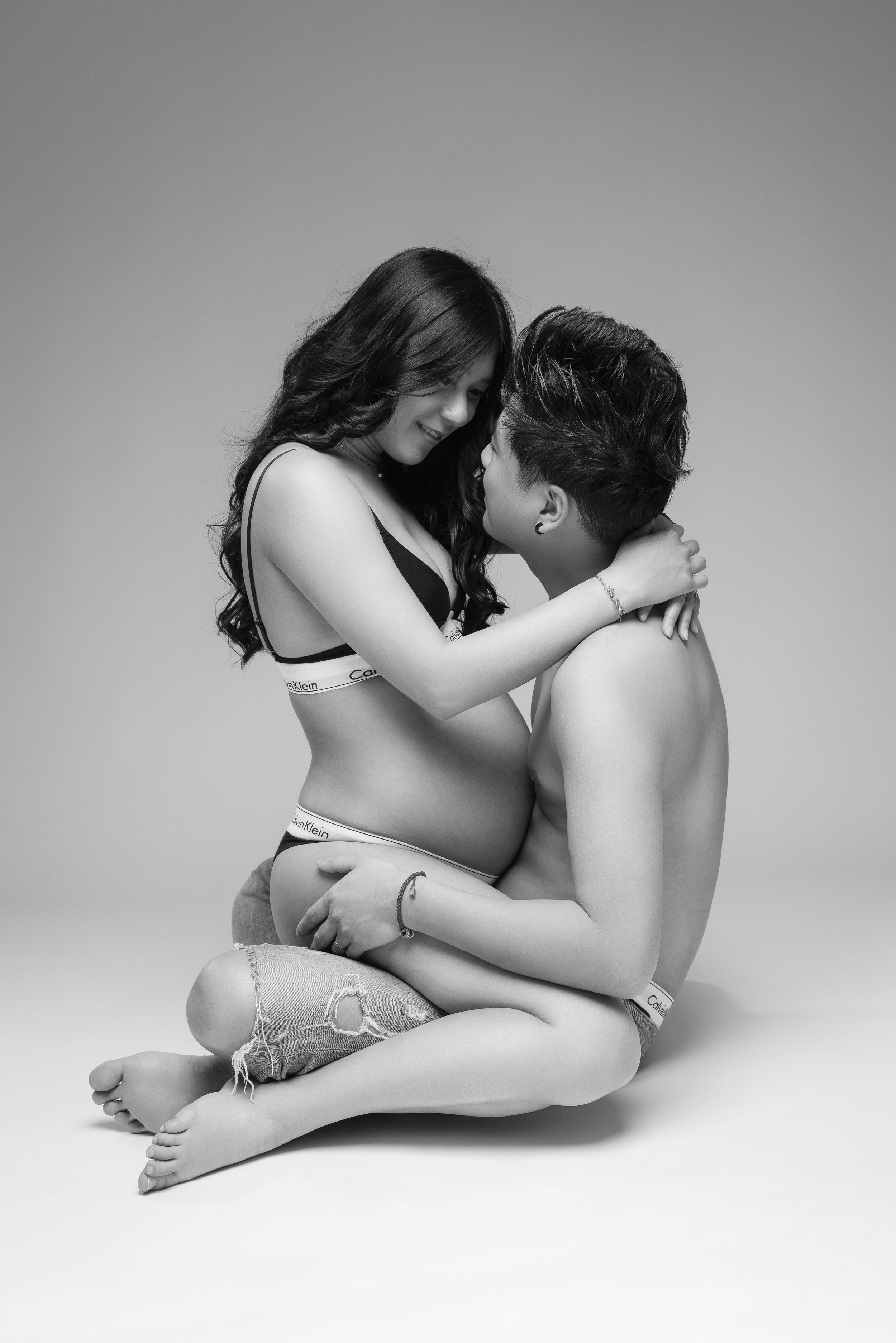 A black and white intimate maternity portrait of a couple embracing while sitting on the floor.