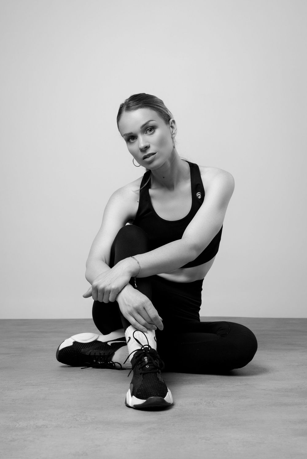 A sequence of black and white photos showing a person in black athletic wear seated on the floor tying shoelaces.