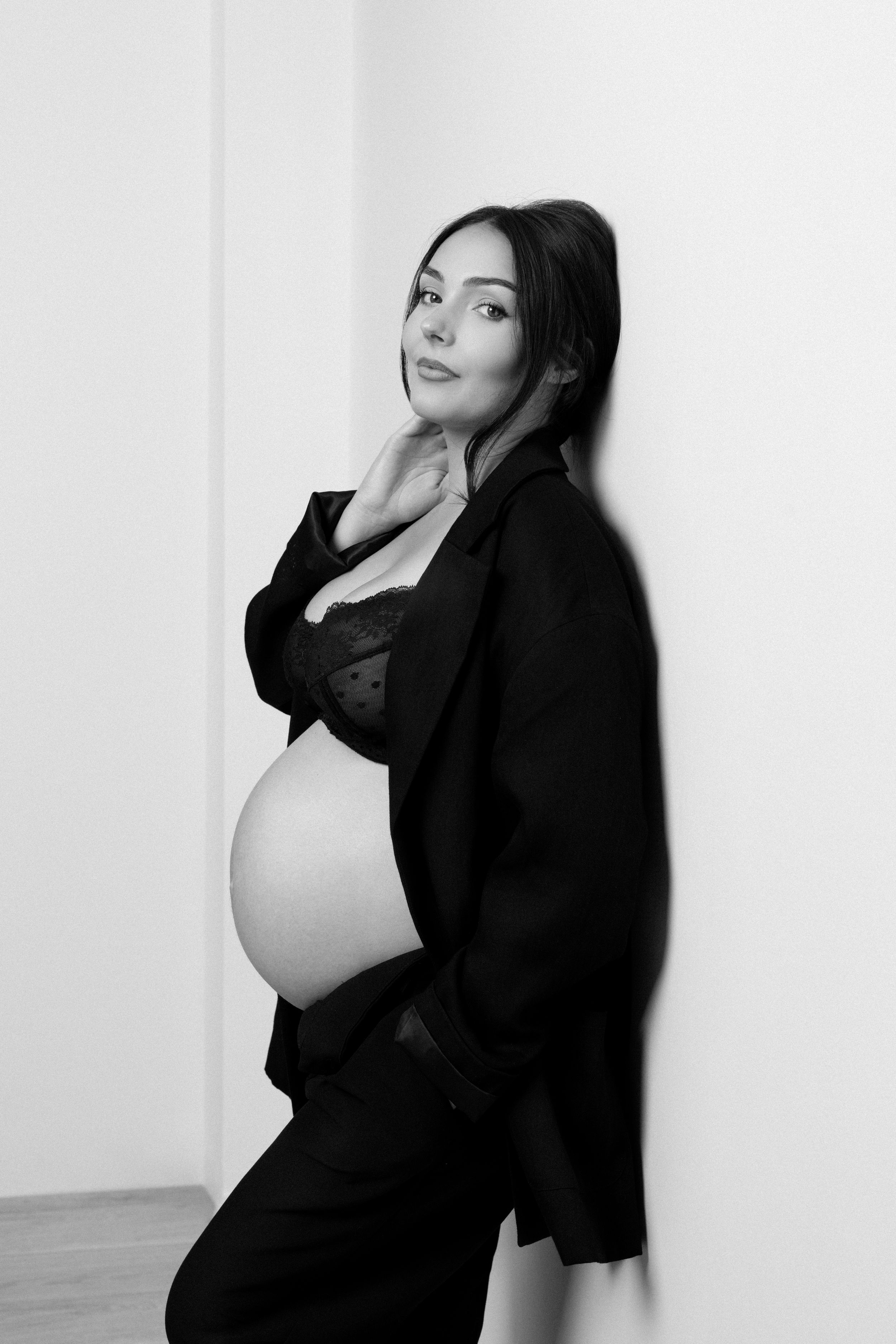 Femme enceinte, tailleur noir appuyée contre le mur