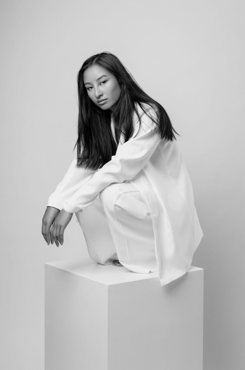 Black and white artistic portrait of a person in flowing white clothing posed elegantly on a white pedestal.