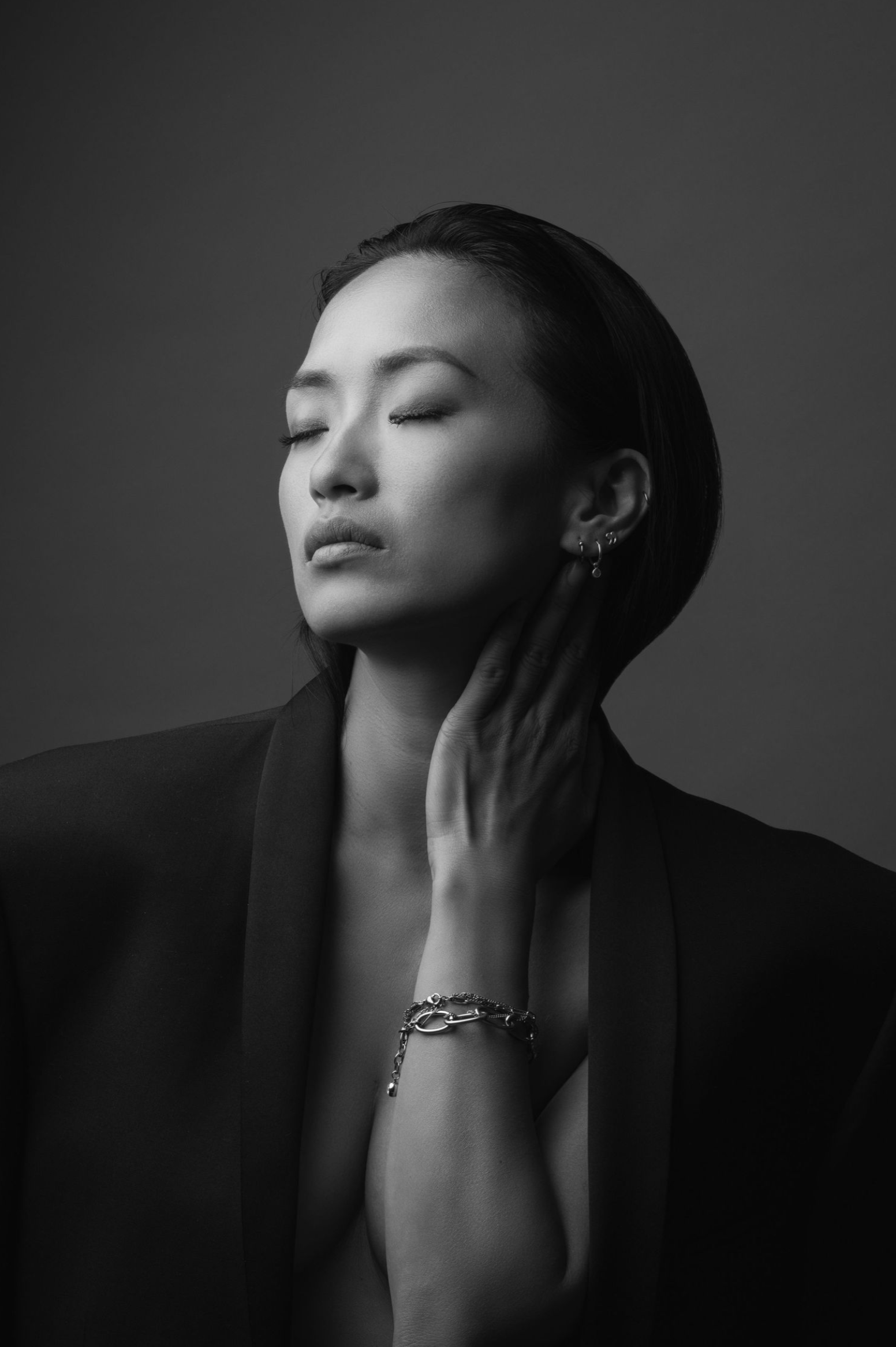 Dramatic black and white portrait with elegant jewelry and peaceful pose against dark background.