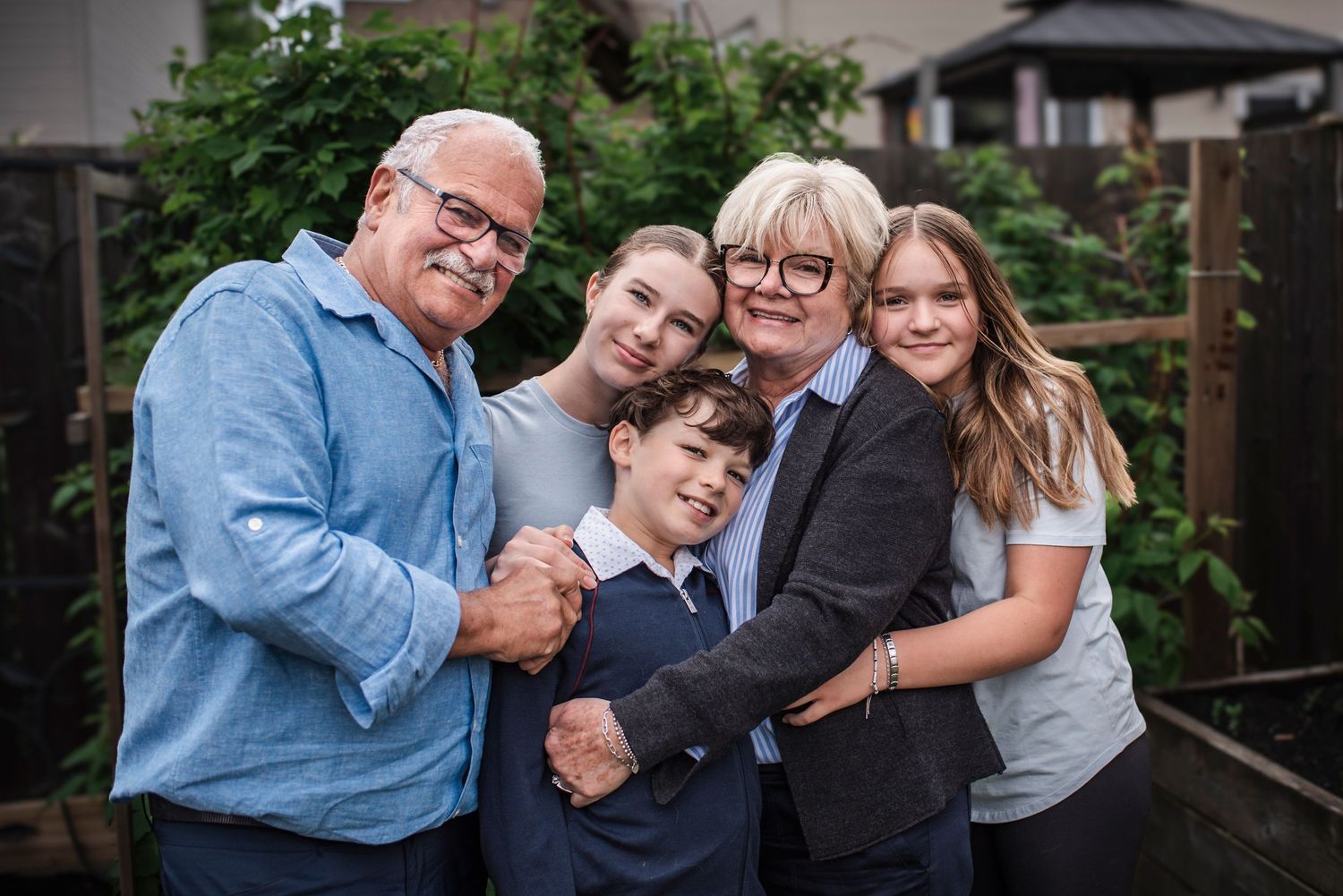 Grandparents with 3 of their grandchildren staying together in front of a green foliage.