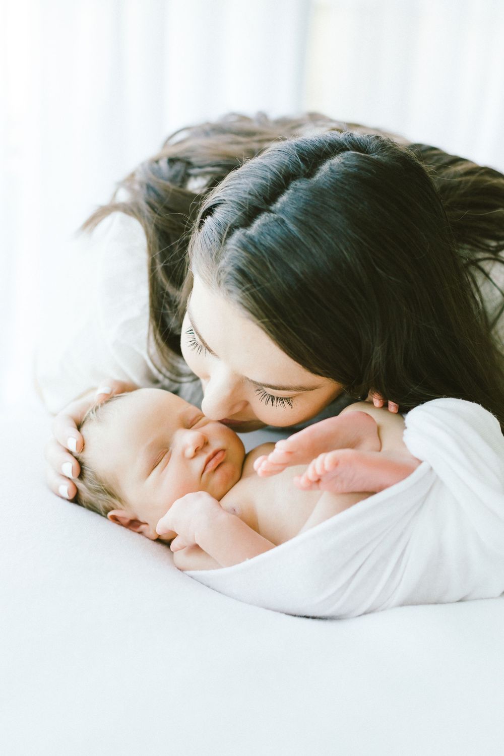 Mother and baby sharing peaceful moment on white bedding.