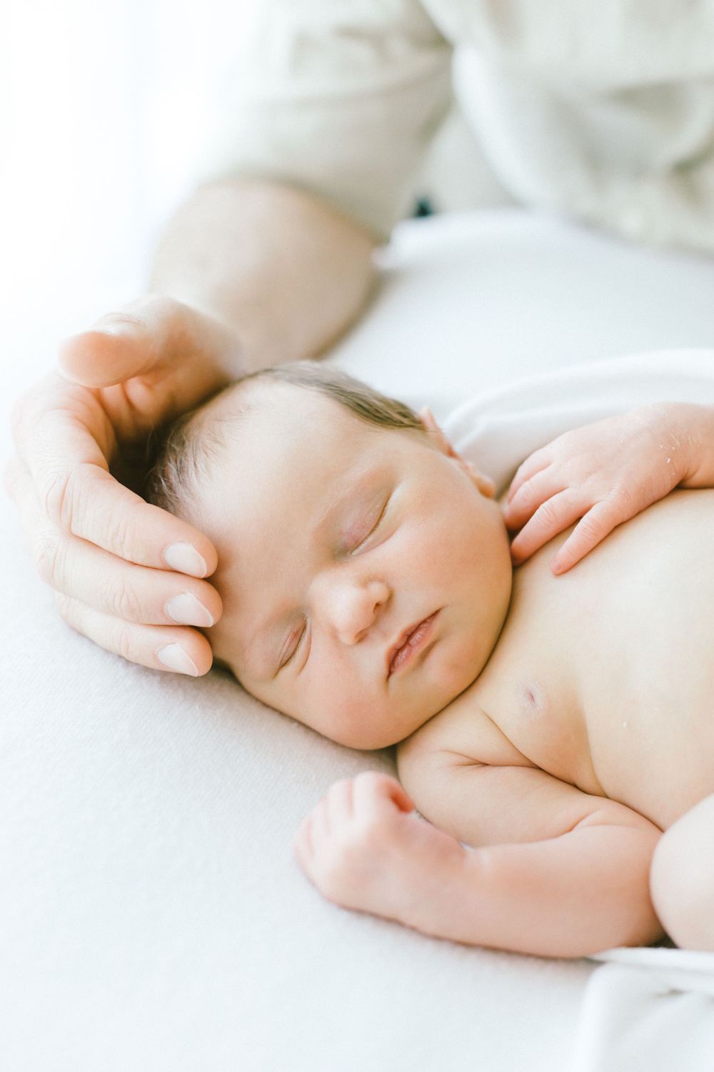 Sleeping newborn baby with delicate features resting on soft white bedding.