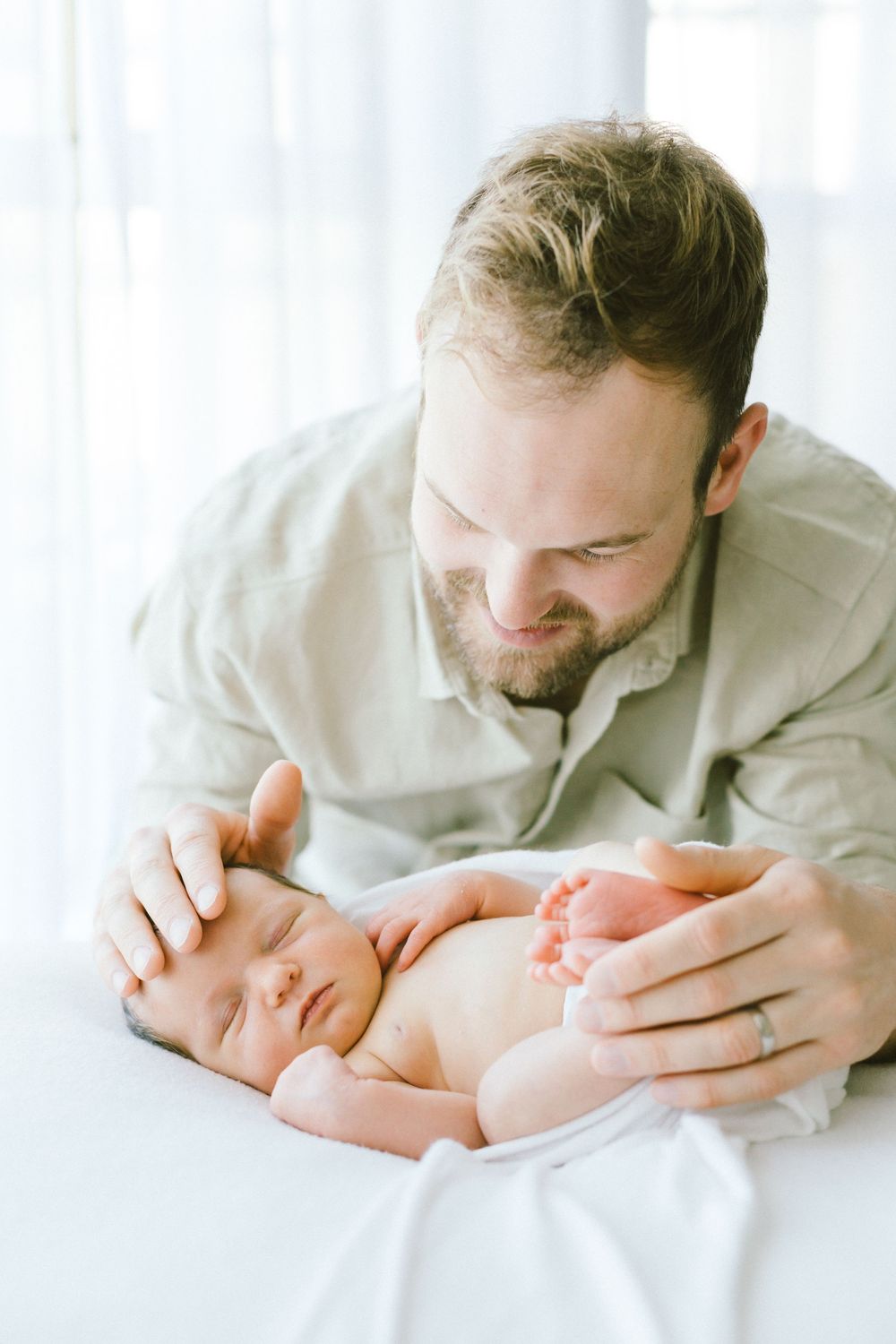 Parent gently touching their sleeping newborn baby in bright natural light.