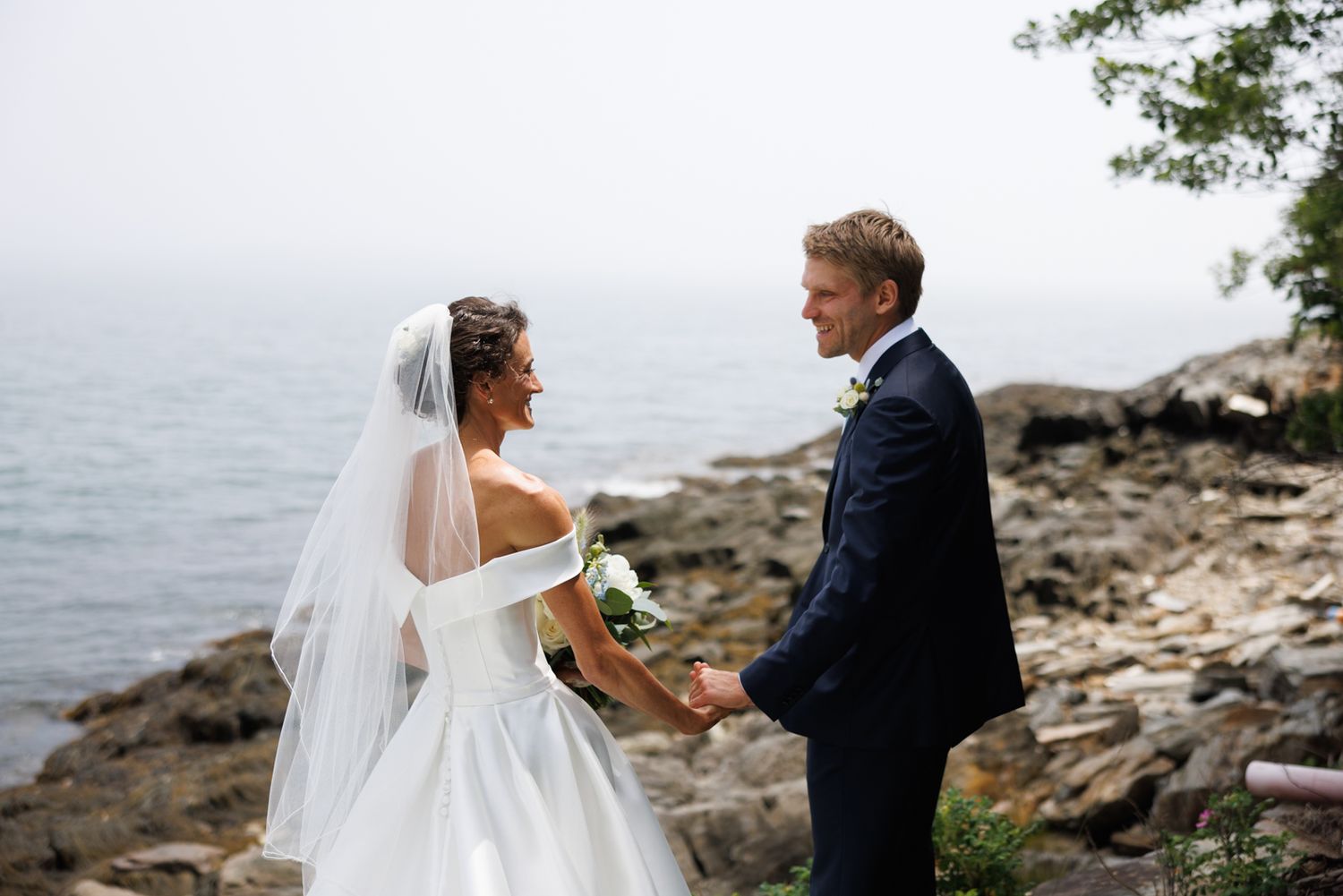 Romantic wedding couple embracing on a rocky coastal shoreline.