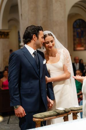 A couple shares an intimate moment during their wedding ceremony inside a historic church with stone columns and arches.