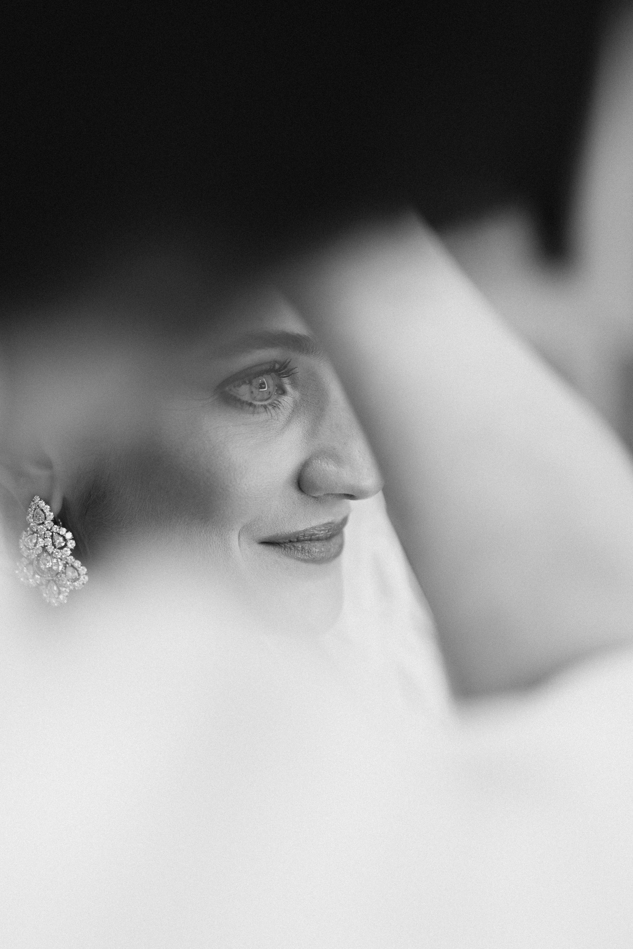 Artistic black and white close up portrait through a veil showing an elegant earring and gentle smile.