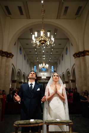 A wedding ceremony takes place inside an elegant church with arched ceilings and a stunning crystal chandelier overhead.