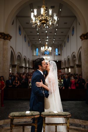 A sequence of wedding photos showing a couple sharing their first kiss as newlyweds in an elegant church with chandeliers.