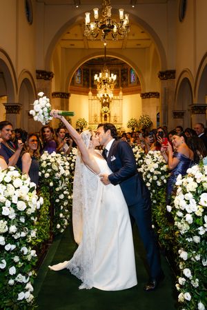 Reception guests celebrate and dance together in an elegant ballroom adorned with crystal chandeliers and white floral arrangements.