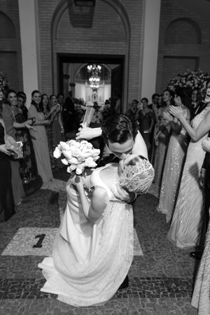 A romantic black and white wedding photo shows a couple sharing a dramatic dip and kiss surrounded by wedding guests.